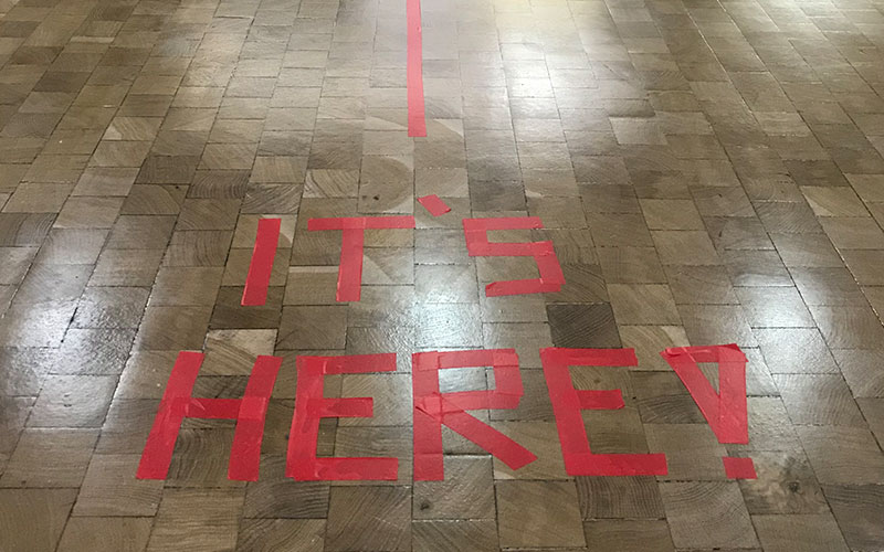 The words It's Here taped in red on the floor